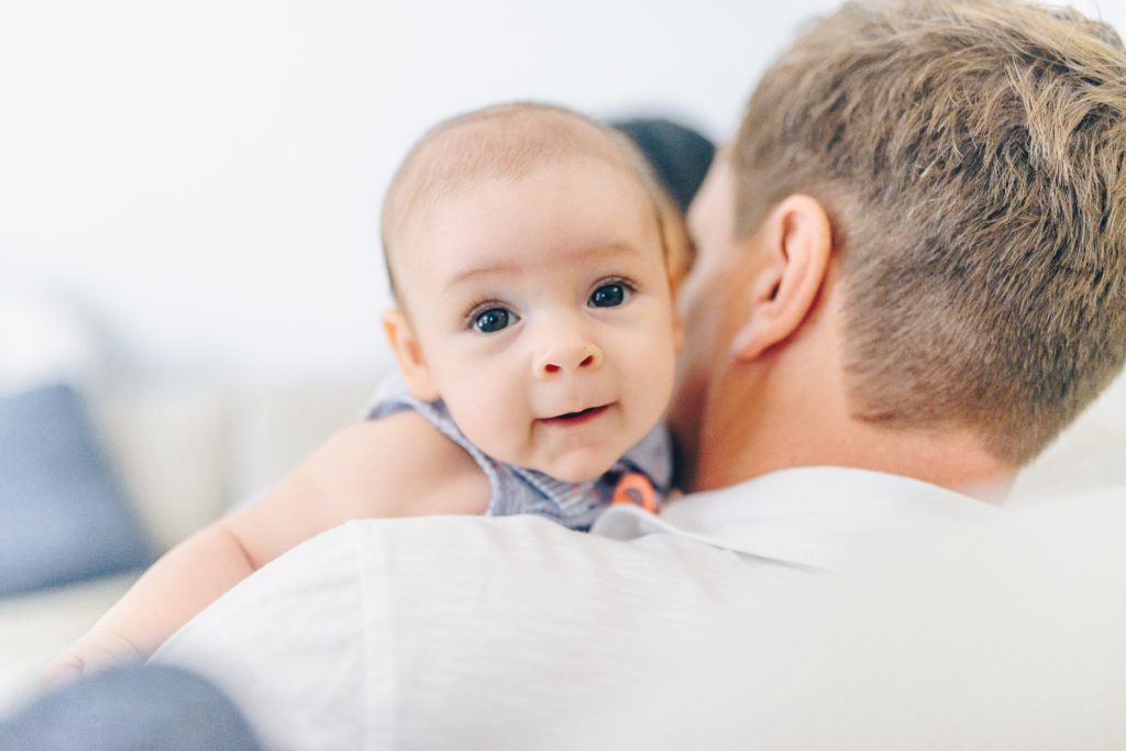 Ein 4 Monate altes Baby wird von seinem Vater ins Bett getragen.