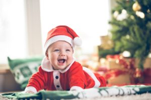 Ein Baby in Nikolaus-Kostüm freut sich über sein Weihnachtsgeschenk.