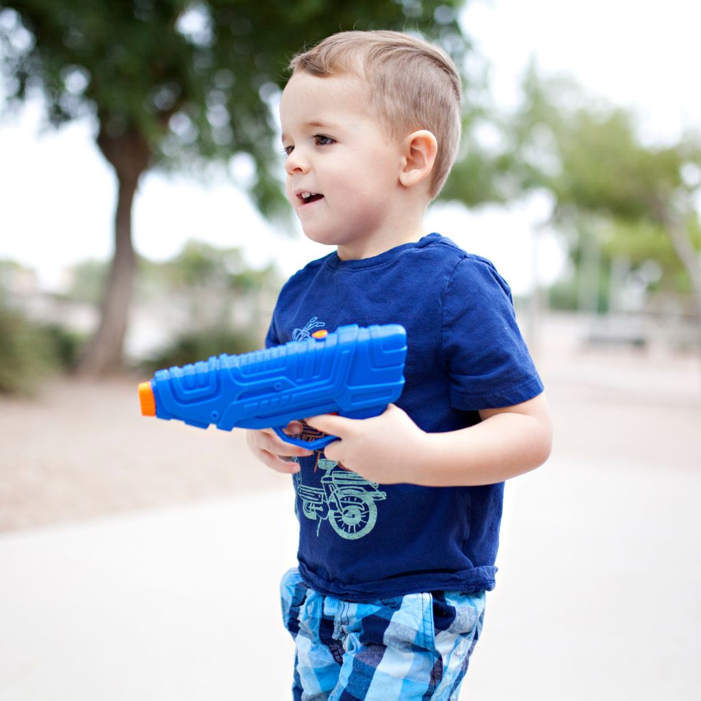 Ein kleiner Junge spielt draussen mit seiner Wasserpistole.