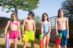 Zwei Jungen und zwei Mädchen in Badekleidung mit ihren Wasserpistolen.
