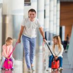 Ein Vater zieht seine zwei Töchter auf ihren Kinderkoffern zum Draufsitzen durch den Flughafen.