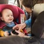 Ein lächelndes Baby in seinem Kindersitz ohne Isofix im Auto.