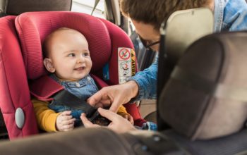 Ein lächelndes Baby in seinem Kindersitz ohne Isofix im Auto.